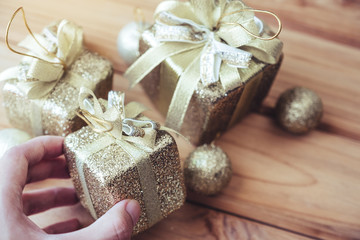 Fototapeta na wymiar Top view image of a hand holding golden present boxes and Christmas decorations on wooden background