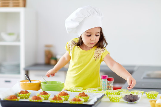 little girl in chefs toque baking muffins at home