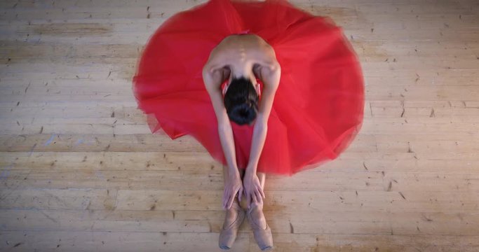Portrait of a beautiful light ballerina, in a lush red dress, sits on a wooden floor, flexible, top view. Concept ballet dancer, slim diet light women, beautiful figure, healthy lifestyle, flexibility