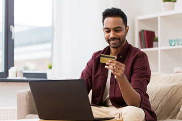 smiling man with laptop and credit card at home