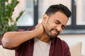 unhappy man suffering from neck pain at home