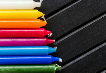 Many colorful candles in a single row and line, black background, candles of vibrant white. yellow,...