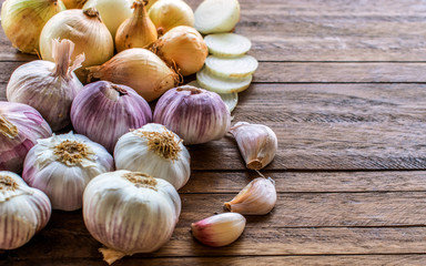 Onions and cut onions, purple whole garlic and garlic cloves on top of a light wooden background, with lots of texture and copy space