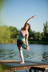 Fototapeta na wymiar Young woman doing yoga in morning park near lake