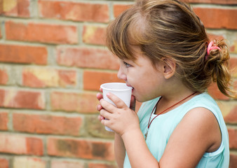A little girl drinks compote from a disposable glass