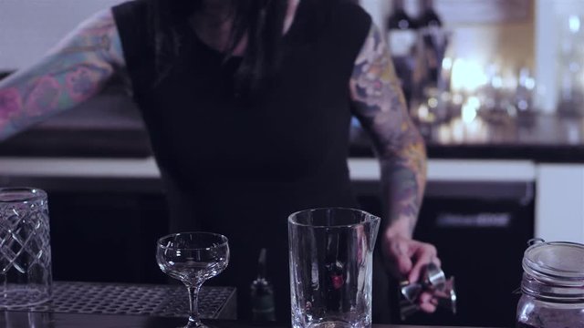 Tattooed bartender lady preparing an alcoholic mixed drink at a bar