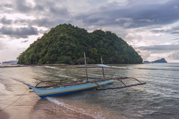 Obraz premium Bangka boat with Depeldel Island view from Las Cabanas beach at sunset in Palawan island, Philippines
