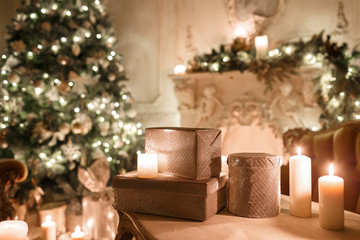 the gifts on the table. Christmas evening by candlelight. classic apartments with a white fireplace, decorated tree, sofa, large windows and chandelier.
