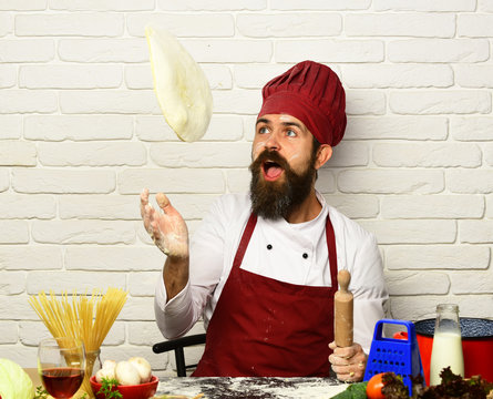 Man with beard throws pizza dough up on white background
