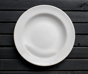 Porcelain or ceramic white plate, ordinary,  on top of a black wooden background tabletop