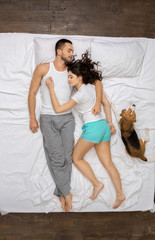 Young couple relaxation on the bed top view with a dog sleeping