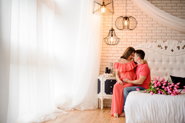 Beautiful pregnant woman and her husband sitting and smiling on the white bed