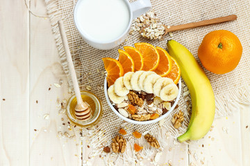 Healthy eating. On the wooden board are muesli, honey in a jar, a banana, an orange, a glass of milk.