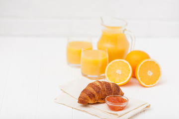 Freshly baked croissant, orange juice, fresh fruits, jam on white wooden background. French breakfast. Fresh pastries for morning. Delicious dessert. Closeup photography. Horizontal banner