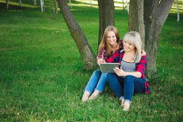 Fototapeta premium Smiling women using tablet ps on a green meadow