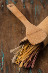 Three coloured dry pasta over wooden top with wooden spoon