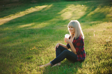 Fototapeta premium Beautiful girl with an orange cocktail on the grass in the park