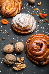 Kanelbulle - swedish cinnamon rolls on a black background with nuts, dry fruits and raisins.