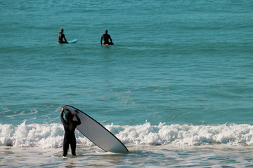 Naklejka premium A man carrying his board to surf with other surfers on the beach of El Palmar, on the coasts of Cadiz, Spain