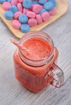 Delicious fresh strawberry, watermelon, banana smoothie in glass transparent mugs with blue and pink candies on the white wood table.
