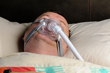 A middle-aged, overweight man wearing a CPAP mask while sleeping in bed