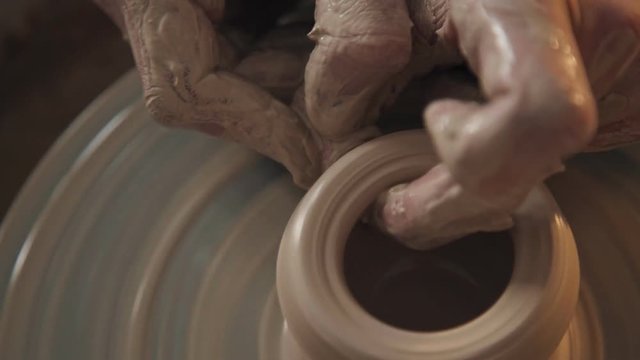 Rotating potter's wheel and clay ware on it (vase): taken from above. Hands in clay. Pottery: male ceramist creates a hand made clay product. Process of rotation of potter's wheel, hands of ceramist