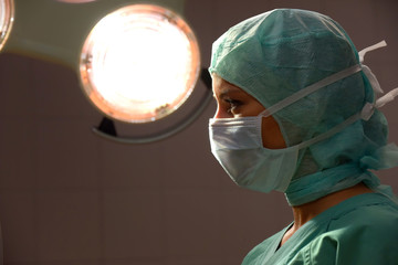 A young woman poses  in an operation theater  fully dressed as a theater nurse with a face mask  and green sterile medical work clothing.