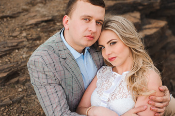 Love, romance and people concept - happy young couple hugging sitting on the edge of a cliff outdoors