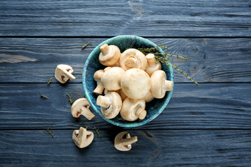 Bowl with fresh champignon mushrooms on wooden table