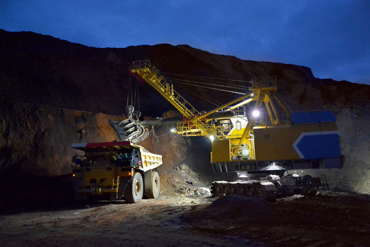 Excavator loads a dumper in a quarry at night