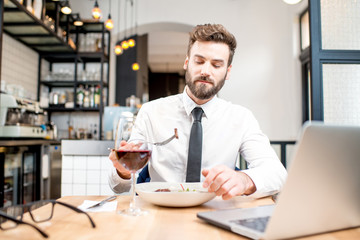 Handsome businessman in white shirt and tie having a dinner with wine and dish sitting at the restaurant