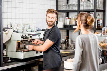 Handsome barista making coffee standing with female client at the bar of the modern cafe interior - obrazy, fototapety, plakaty