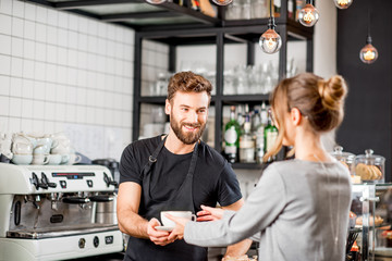 Handsome barista giving a coffee to the female client at the bar of the modern cafe
