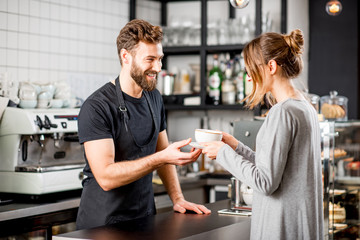 Handsome barista giving a coffee to the female client at the bar of the modern cafe - obrazy, fototapety, plakaty