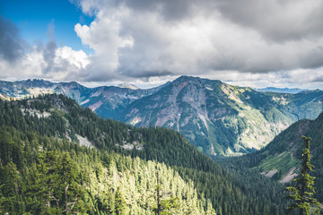 Rocky mountains covered with green forest with blue sky and white clouds on the background