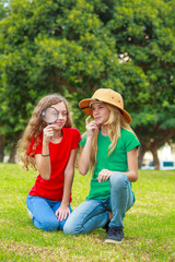 Two school girls exploring the nature with magnifying glass