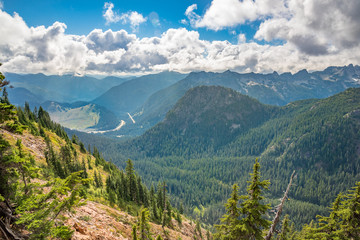 Rocky mountains covered with green forest with blue sky and white clouds on the background