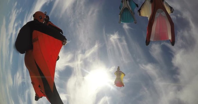 A base jumper in a wingsuit leaping off a from a rocky cliff, gliding down over a green landscape
