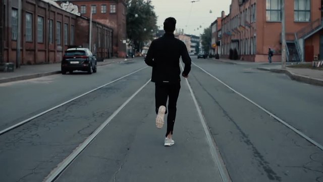 Sportsman running between tram tracks. Background shot. Slow motion. Concept of strong individuality and confidence.