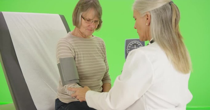 An older patient gets her blood pressure checked by her doctor on green screen. On green screen to be keyed or composited. 
