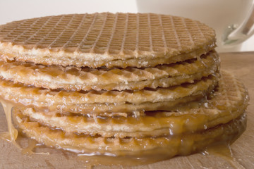 round cookies or wafers with a layer of caramel lies on a rough pile on a wooden board, mug of clear glass with milk