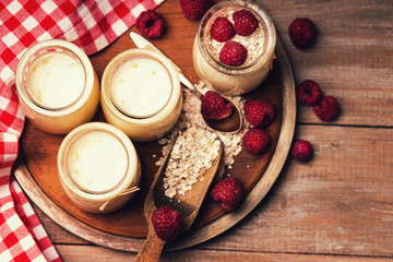 Jars with yogurt, raspberries, wooden scoop, spoon and oat flakes 