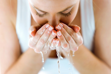 Fototapeta premium Piękna młoda kobieta do mycia twarzy rozpryskiwania wody w domowej łazience.