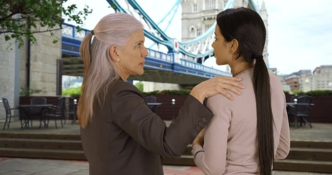 Kind mature woman executive giving young woman business advice near Tower Bridge