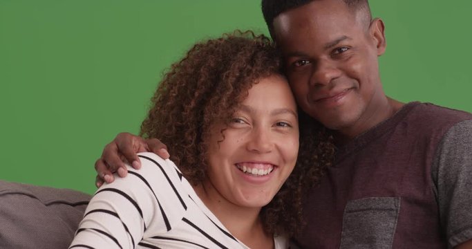 Smiling happy black couple posing for portrait on their sofa on green screen. On green screen to be keyed or composited. 