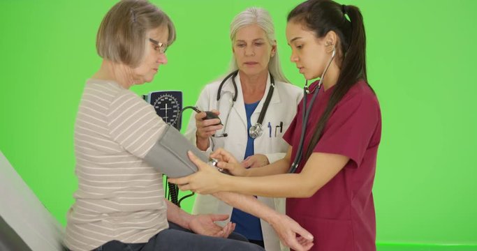 Doctor training nursing student to take blood pressure with cuff on green screen. On green screen to be keyed or composited. 