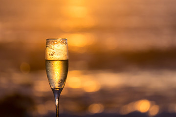 A frosty glass of bubbly champagne with a golden bokeh backlit sunset background is ready for a...