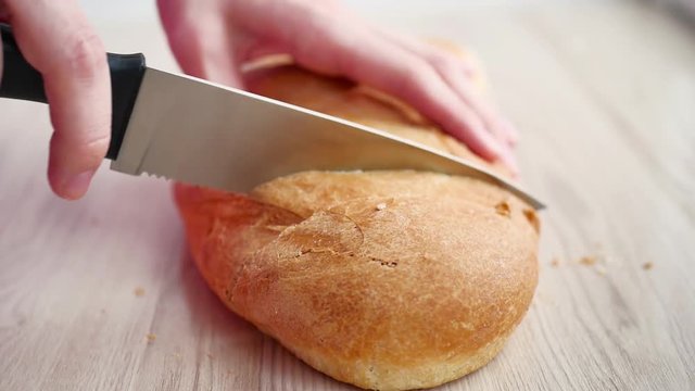 Female hands cutting bread on wooden board, close-up, selective focus.
