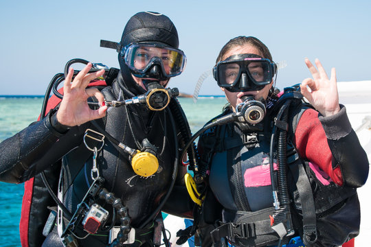 two happy divers in wetsuits and masks with octopus in mouthes on the background of azure sea show ok . happy girls in wetsuits. scuba diving. diving. divers