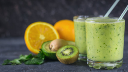 Two glass glass filled with the smoothie of avocado on a black wooden table with fruits. Diet vegetarian food.